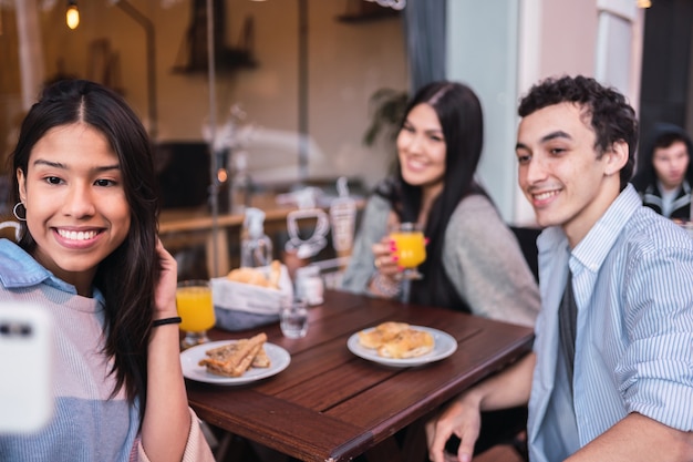 Gruppo di amici che prendono un selfie, seduti all'aperto in un bar.