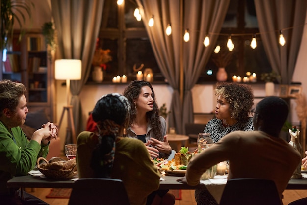 Group of friends talking to each other at dining table during a meeting at dinner party at home