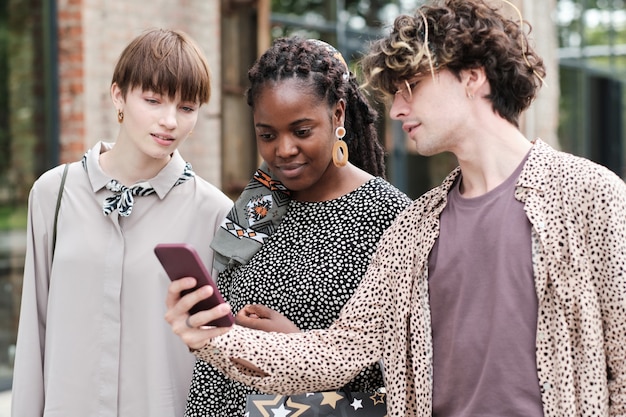 Group of friends using mobile phone together while walking in the city