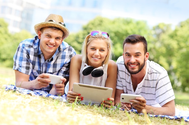 a group of friends using tablet and smartphones in the park