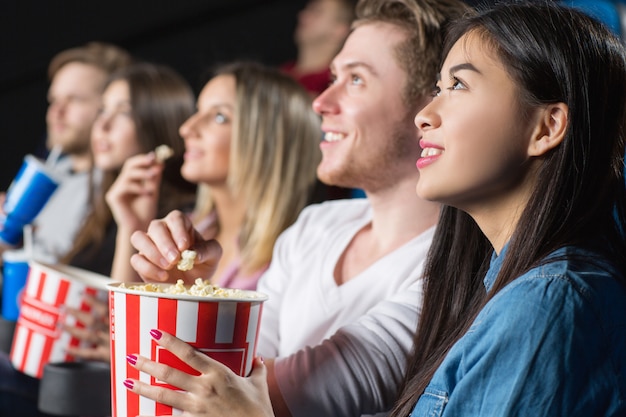 Gruppo di amici che guardano film mangiando popcorn al cinema locale