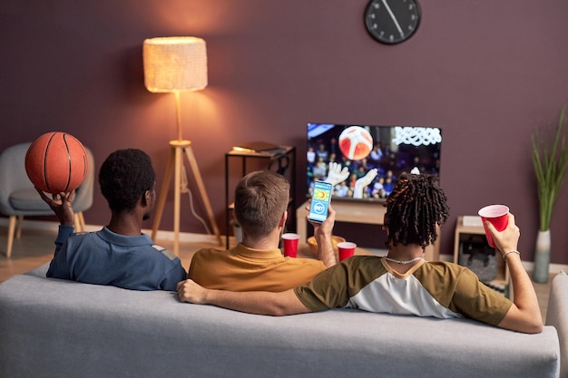 Group of friends watching sports match at home and drinking beer