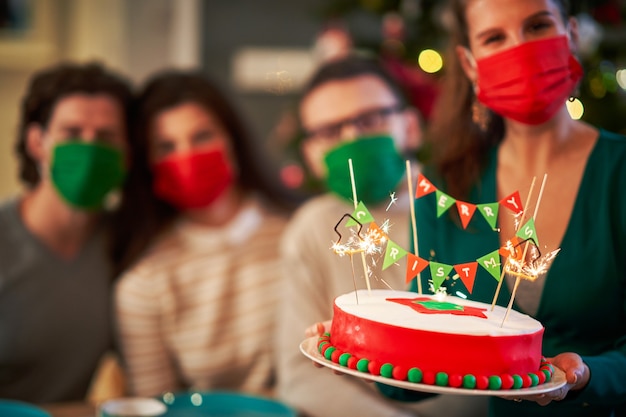 Foto gruppo di amici che indossano maschere protettive mentre celebrano il natale a casa godendosi la torta x-mass