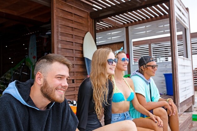 Foto gruppo di amici che indossano costumi da bagno che si siedono con i surf sulla spiaggia