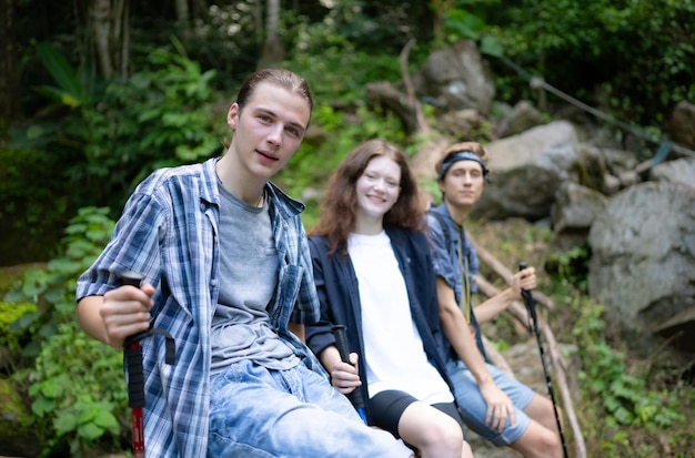 Group of friends with backpacks and sticks sitting on a fallen tree Take a break during the hike