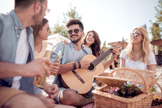 Gruppo di amici con la chitarra che fanno picnic sulla spiaggia