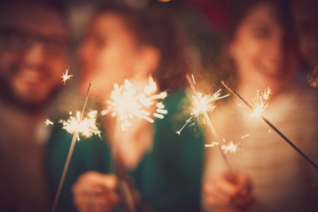 Photo group of friends with sparklers celebrating christmas and new year at home