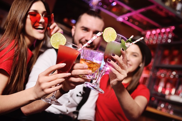 Group of friends-young guy and two cute girls having fun at a party holding cocktails