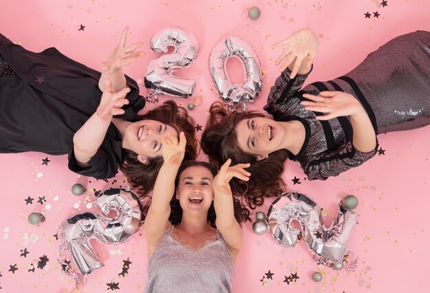 A group of girlfriends are having fun at a Christmas party, lying on a pink background with balloons from the numbers 2022, top view.