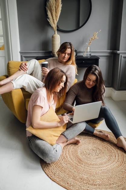 A group of girlfriends communicate with a friend via a video conference on a laptop