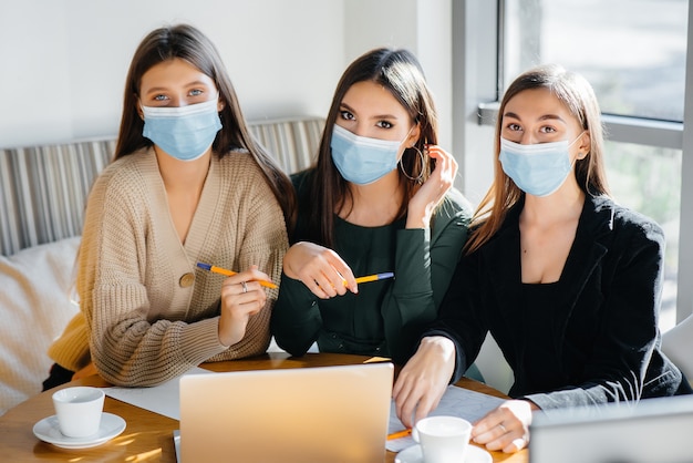 A group of girls in masks sit in a cafe and work on laptops. Teaching students.