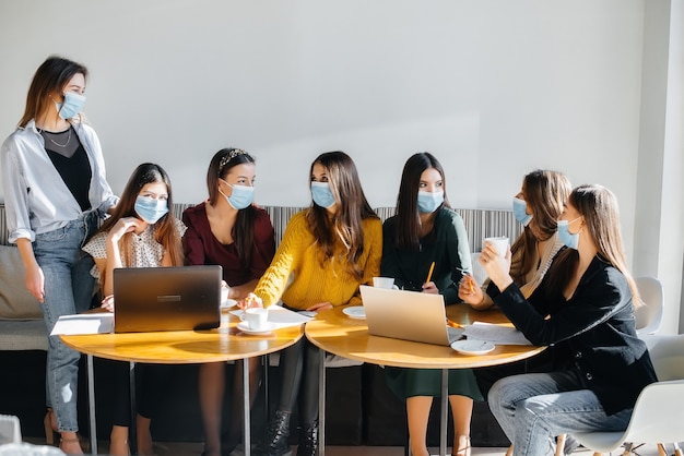 A group of girls in masks sit in a cafe and work on laptops. Teaching students.