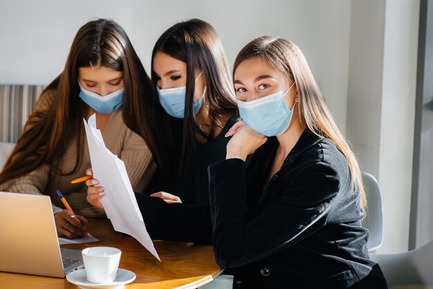 A group of girls in masks sit in a cafe and work on laptops. Teaching students.