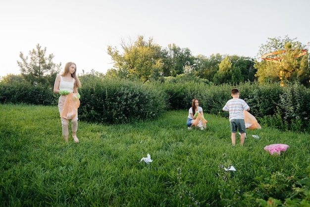 A group of girls with children at sunset are engaged in garbage collection in the park. Environmental care, recycling.