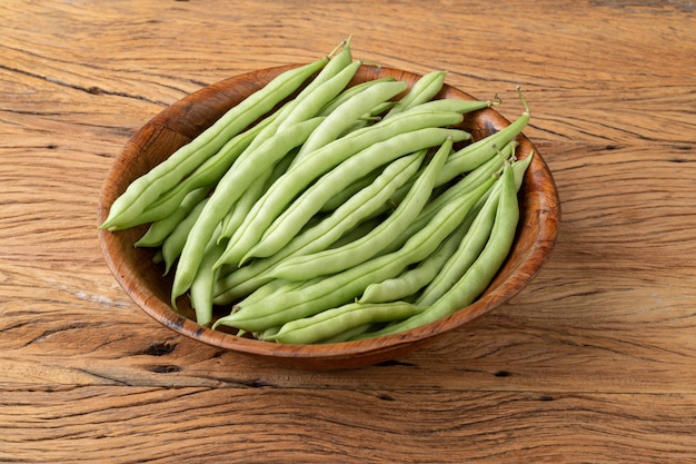 A group of green bean pods in a bowl over wooden table.