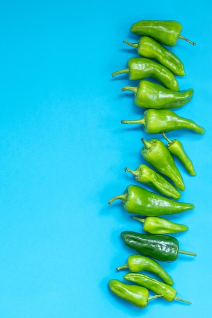 Photo group of green peppers of different sizes on a blue background vertical photo