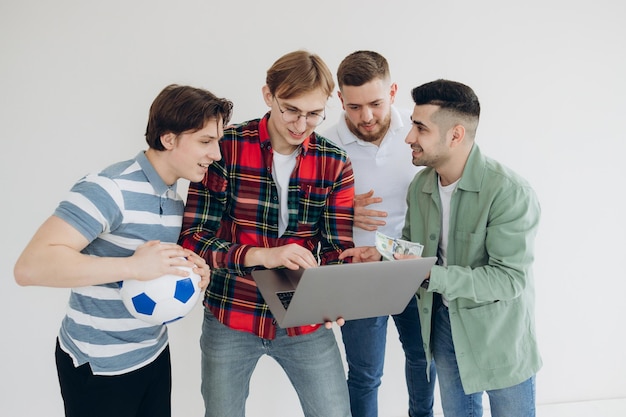 Group of guys male friends looking at sports betting coupon on\
laptop decide which team to bet on gambling concept sports betting\
online betting