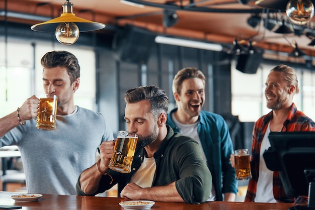 Group of handsome young men in casual clothing enjoying beer and communicating