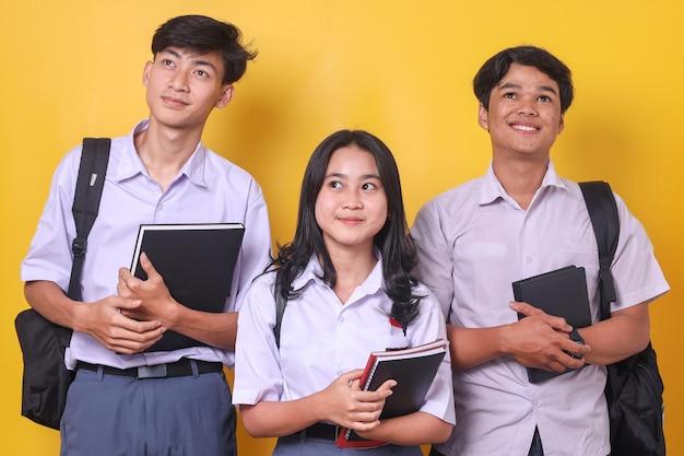 Group of happy Asian students holding book carrying backpack and standing over yellow background wh