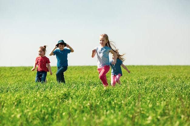 男の子と女の子の幸せな子供たちのグループは、晴れた夏の日に芝生の上の公園で実行されます民族の友情平和優しさの子供時代の概念