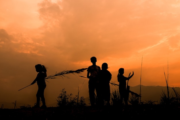 夕日、シルエットで牧草地で遊んでいる幸せな子供たちのグループ