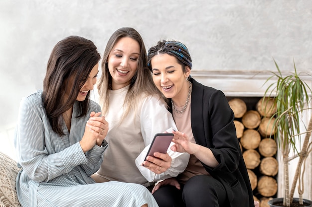 Amici femminili felici del gruppo che chiacchierano navigando in internet usano lo smartphone sorridente avendo emozione positiva