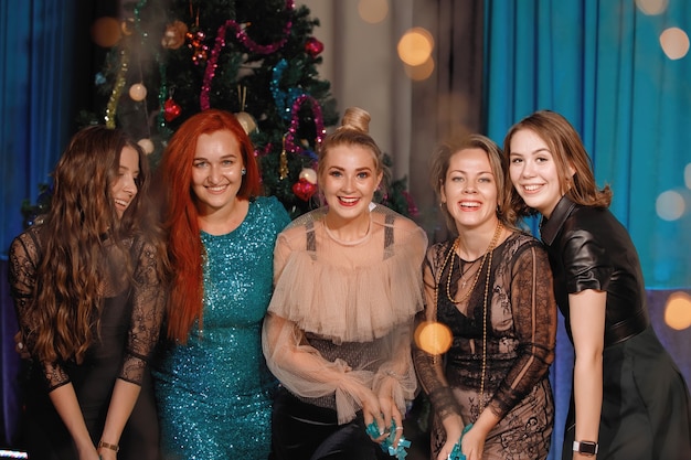 Group of happy friends dancing near the Christmas tree. Women laugh, rejoice.