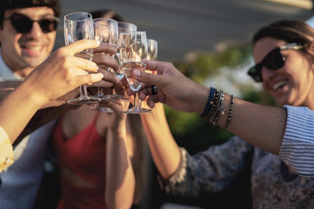 Group of happy friends drinking and toasting champagne outdoors in the terrace - Friendship concept with young people having fun together celebrating in the garden