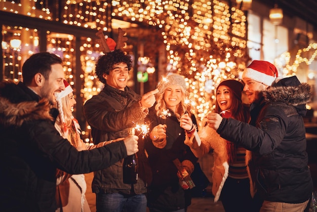 group of happy friends having fun with sparklers on night christmas party.