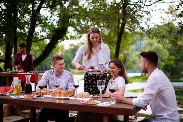 group of happy friends having picnic french dinner party outdoor during summer holiday vacation  near the river at beautiful nature