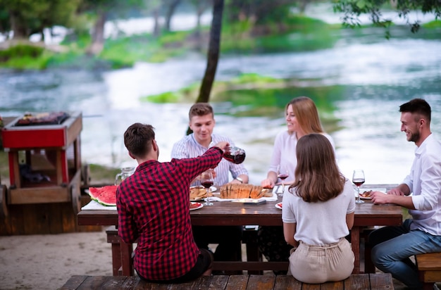 group of happy friends having picnic french dinner party outdoor during summer holiday vacation  near the river at beautiful nature