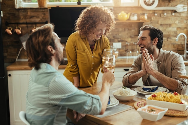 ダイニングテーブルで昼食時にワインを飲みながら笑って楽しんでいる幸せな友人のグループ。