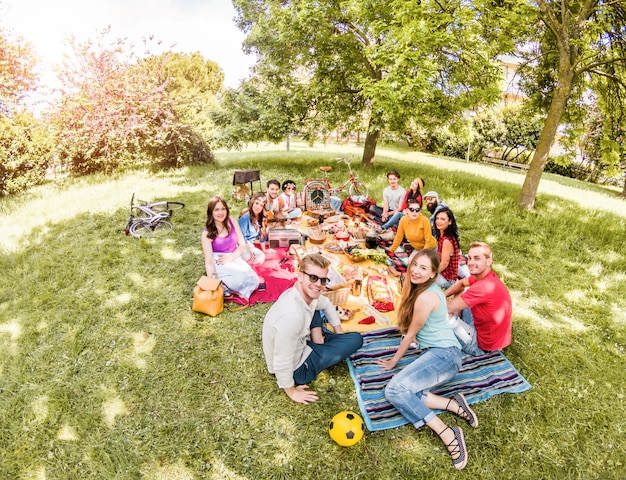 Gruppo di amici felici che fanno picnic sul parco pubblico all'aperto - giovani che bevono vino e che ridono in natura