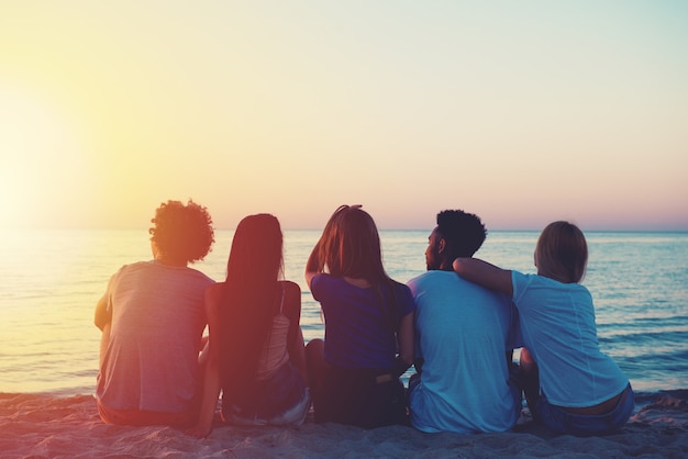 Группа счастливых друзей, отдыхающих на пляже во время заката