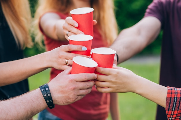 Group of happy friends relaxing on nature with red cups of alcohol.