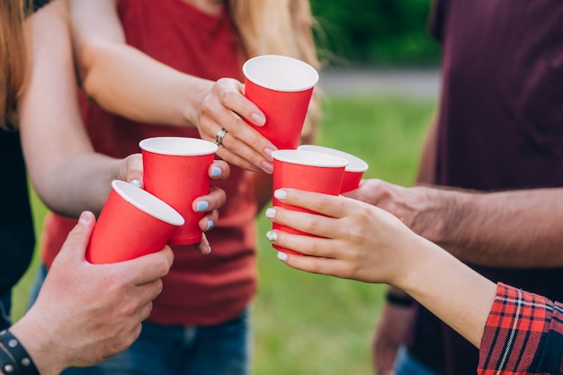 Group of happy friends relaxing on nature with red cups of alcohol.