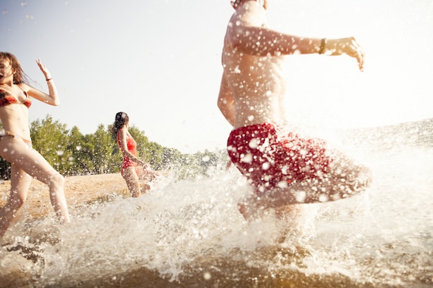 Group of happy friends running in to water - active people having fun on the beach on vacation - Tourists going to swim