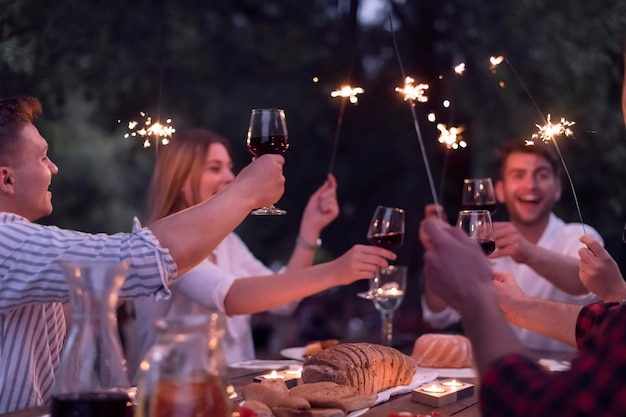 group of happy friends toasting red wine glass while having picnic french dinner party outdoor during summer holiday vacation near the river at beautiful nature