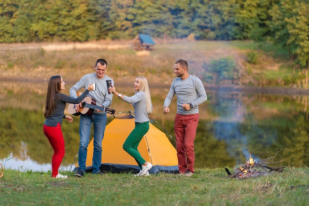 Group of happy friends with guitar, having fun outdoor, dancing and jumping near the lake in the park