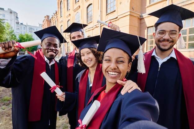 Group of happy graduated students making selfie portrait against their university