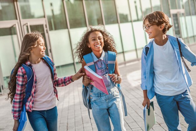 Group of happy kids walking and laughing together with backpacks near school building