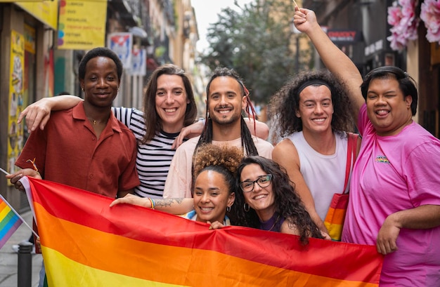 Photo group of happy lgbtq people are posing with a rainbow flag before a gay parade mado in madrid city