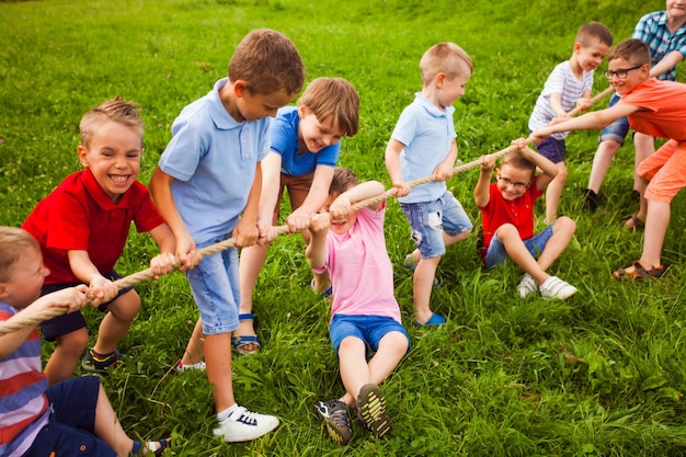 The group of happy little children are playing tug of war outside on the grass