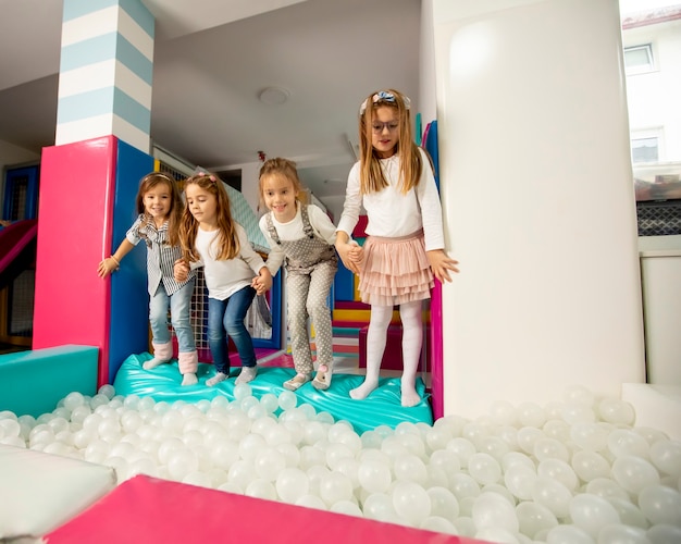 Group of happy little girls jumping into ball pit