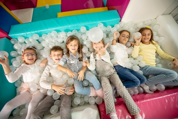 Group of happy little kids in ball pit smiling happily at camera while having fun