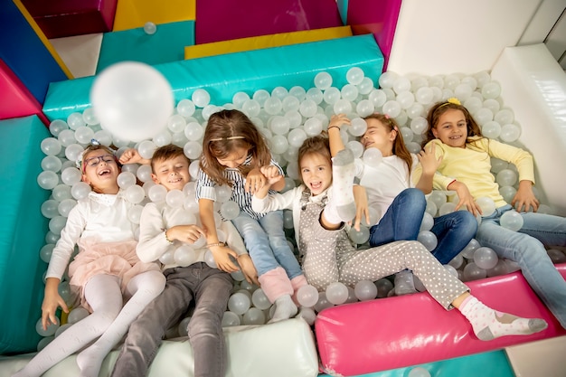 Photo group of happy little kids in ball pit smiling happily at camera while having fun