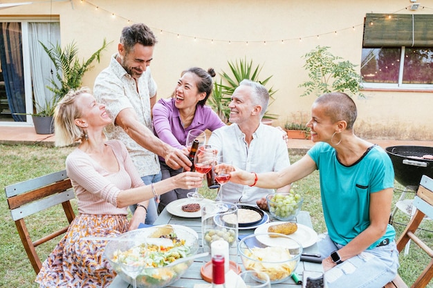 Group of happy middleaged men and women toasting wine glasses\
at dinner event at house backyard