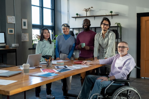 Group of happy modern economists standing by table with financial papers