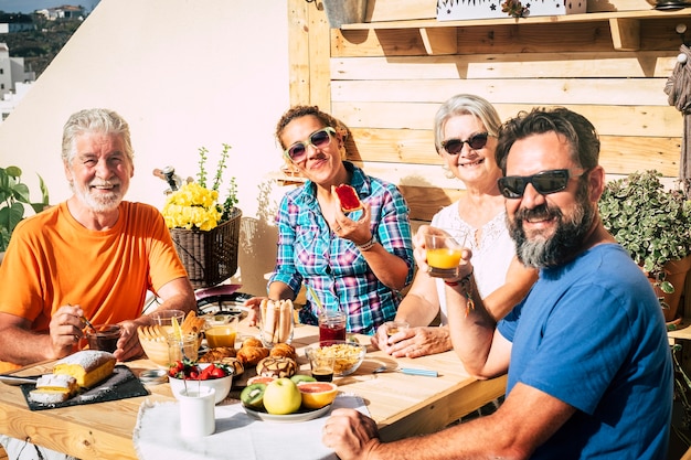 Группа счастливых людей, завтракающих дома на террасе вместе с любовью - смех, сын, бабушка и дедушка едят и пьют - пара пожилых людей, женатых и взрослых