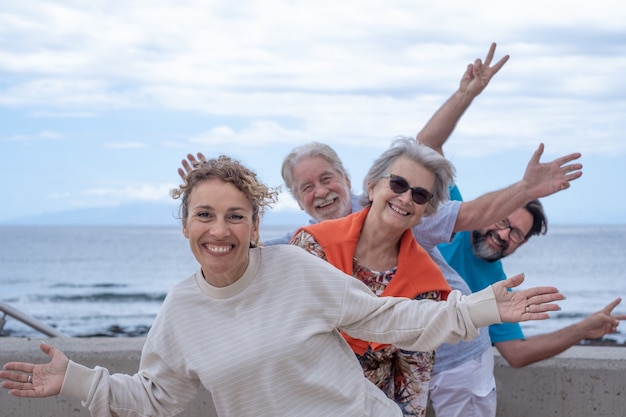 Group of happy people having fun together at sea, cloudy sky. Multi generation family gesturing positivity and freedom